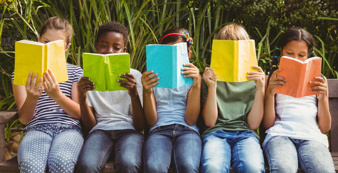 Crianças e jovens sorrindo lendo livros em uma biblioteca comunitária.
